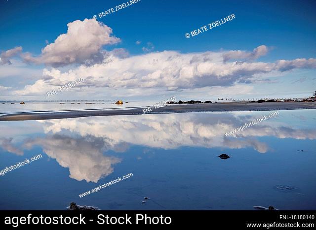 Dramatic cloudy sky reflected on water surface on the beach of Neukirchen (Schleswig-Flensburg district) on the Flensburg Fjord