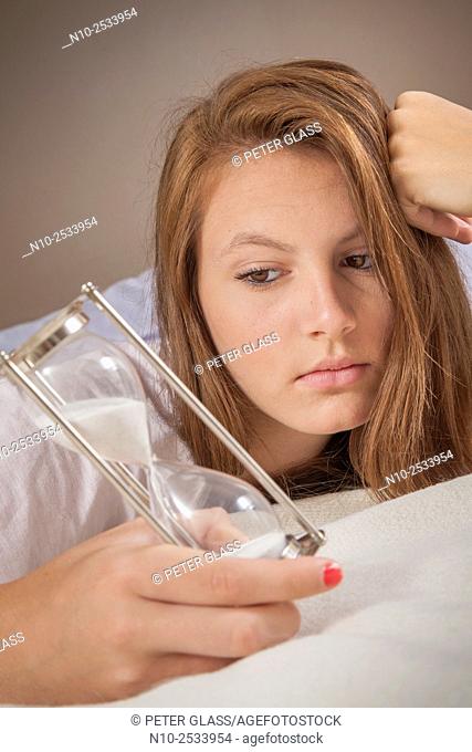 Teenage girl on her bed with an hourglass