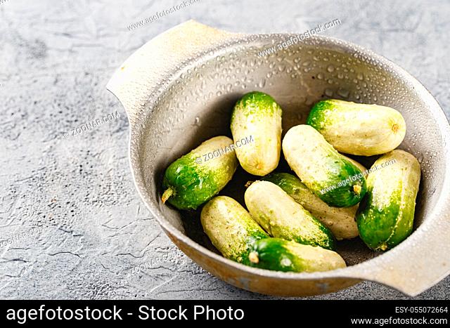 Baby cucumbers with unusual coloring in metal bowl on gray background. Close up