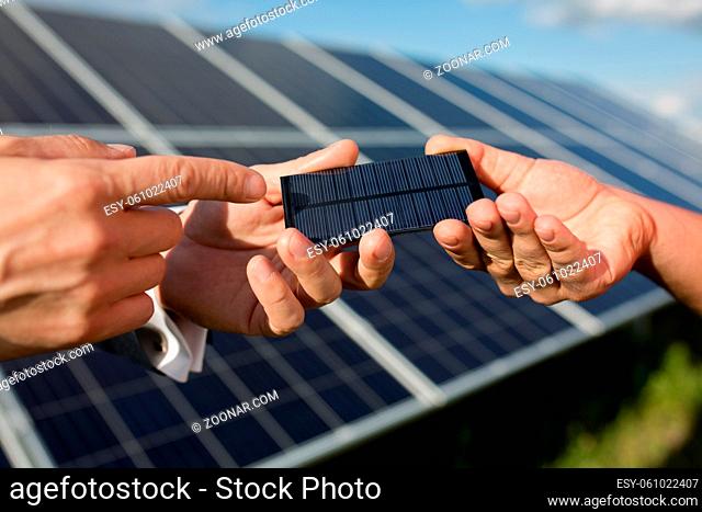 Solar energy, two hands holding photovoltaic item. Solar panels in the field, close yp view on photovoltanic detail