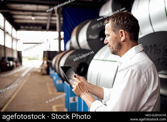 Male owner using digital tablet while standing in factory