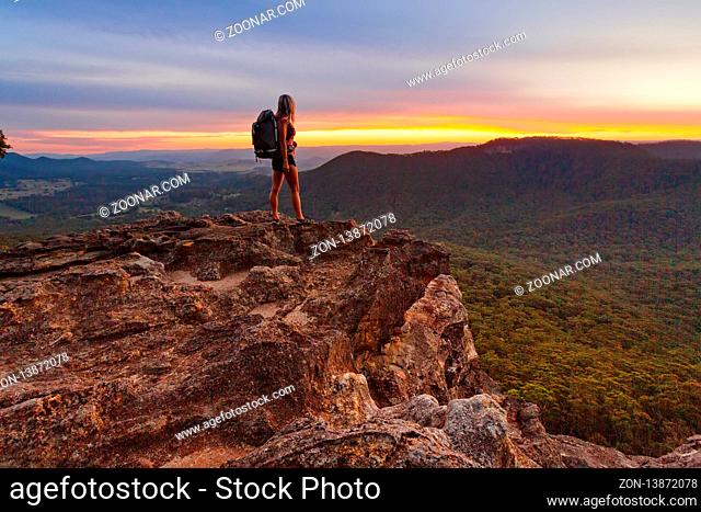 Hiker watching the last light and fiery sunset colours fade as she watches lingering on with hope it will not end, but alas dusk and night will be swiftly upon...