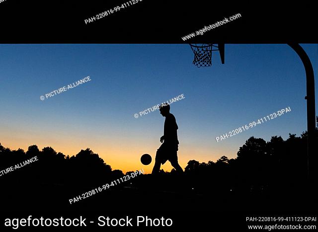 16 August 2022, Bavaria, Nuremberg: A youth plays basketball at a public hoop under a bridge at dusk. Photo: Daniel Karmann/dpa