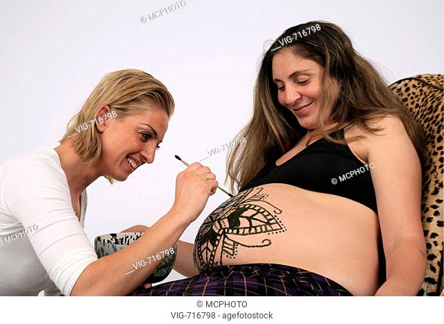 young woman is painting henna-tattoo on pregnant belly, Germany  - GERMANY, 03/09/2007