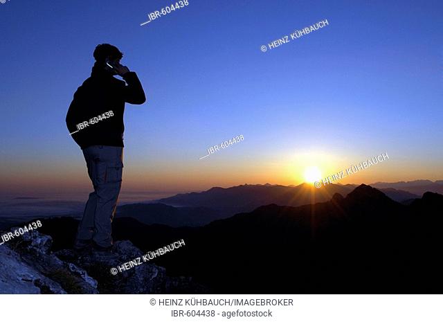 Man with mobile phone at sunrise on a mountain top, Breitenstein Mountain, Bavarian foothills, Wendelstein Group, Upper Bavaria, Bavaria, Germany