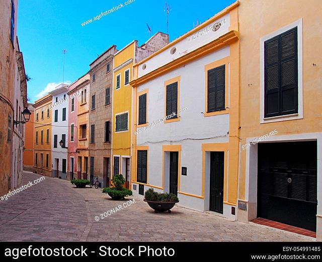a scenic view of an empty street of bright painted yellow traditional houses in ciutadella menorca with bright blue summer sky