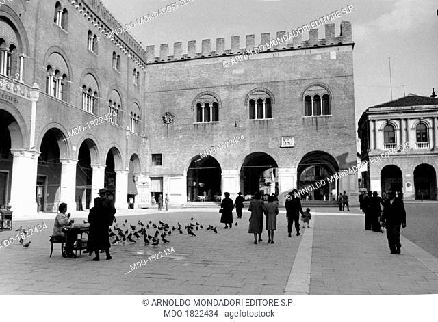 A girl selling corn for pigeons on piazza dei Signori facing the palazzo del Podestà and the palazzo dei Trecento. Treviso, April 1954