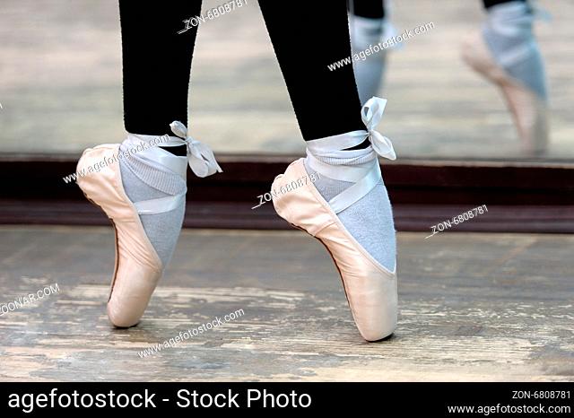 Close up view to ballerinas legs in white pointes on wooden floor in point position