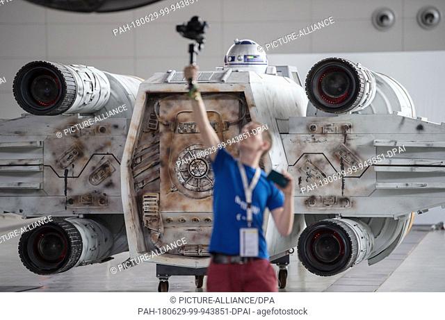 29 June 2018, Germany, Stuttgart: A journalist filming the reconstruction of an ""X-Wing"" spaceship from the film saga Star Wars during the set-up of the pop...