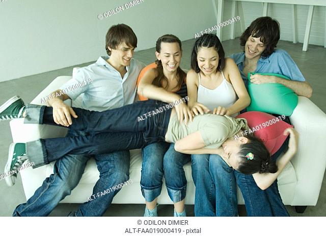 Group of young friends sitting on sofa, one lying across legs of others