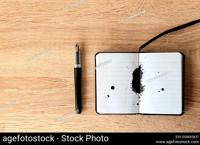 Fountain pen on a notebook. Black ink splash. Wooden table. Copy space