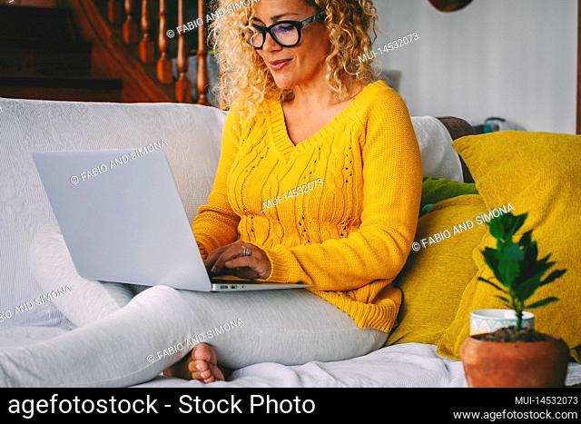 Pretty middle age woman writing on laptop and smiling. Single lady using computer alone at home. Blonde female adult enjoy leisure time with wireless notebook...