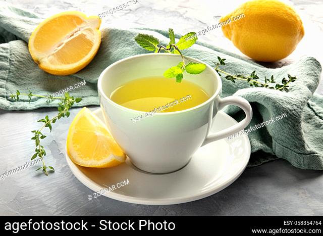 A closeup of a cup of green tea with lemons and herbs