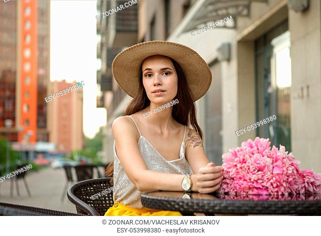 Beautiful, happy brunette girl wearing a hat and a yellow skirt with a bouquet of flowers in the city
