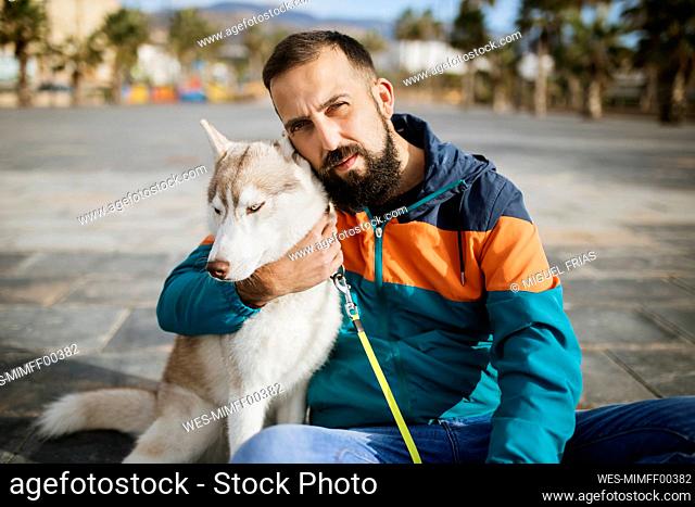 Bearded man embracing Siberian Husky while sitting on road