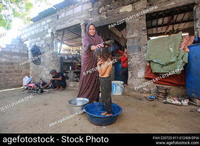 25 July 2022, Palestinian Territories, Khan Yunis city: A Palestinian girl takes a bath in a plastic bowl, inside his sheet metal home