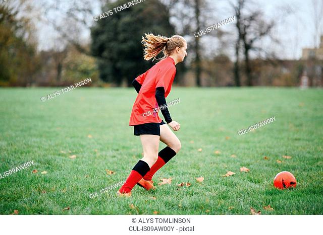 Teenage female soccer player practicing with soccer ball in park