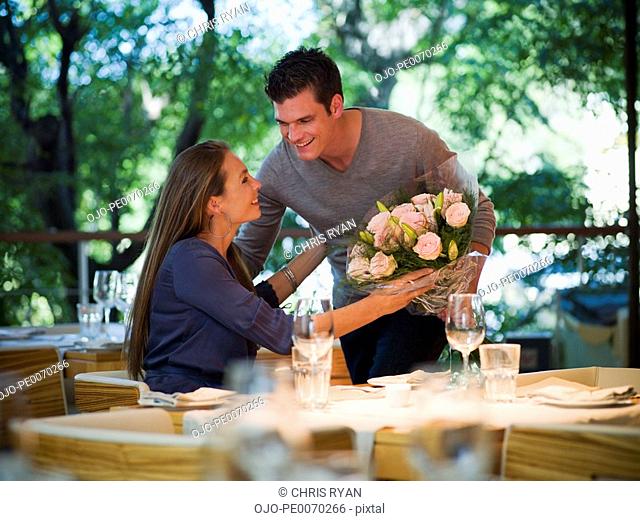 Man giving flowers to woman at restaurant table