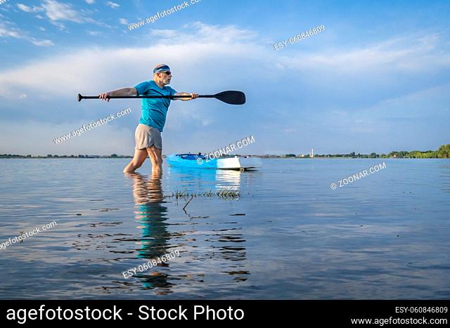 senior paddler is stretching and warming up before morning workout on a stand up paddleboard - Boyd Lake State Park in northern Colorado