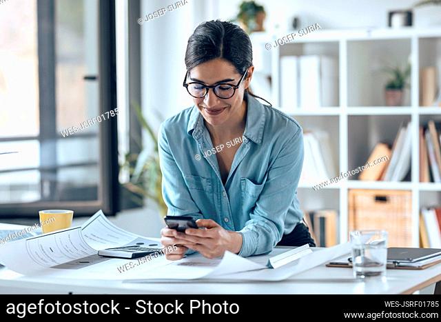 Smiling businesswoman using smart phone in small office