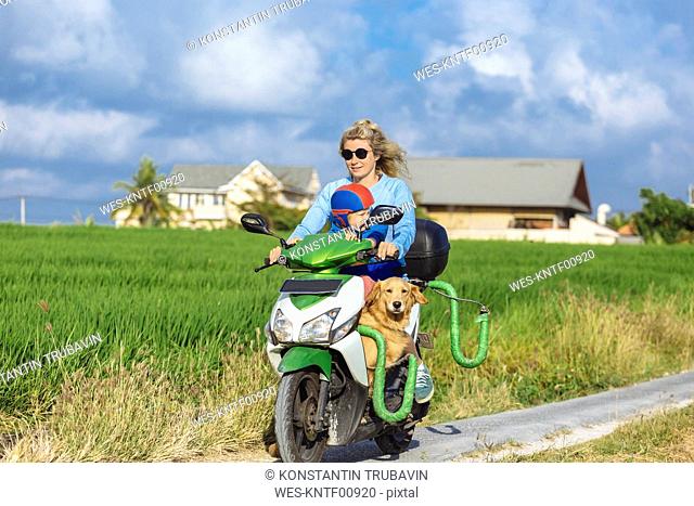 Woman with child and dog riding motor scooter on country lane