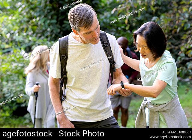 Two middle-aged male and female hikers stopping to look lady's fitbit
