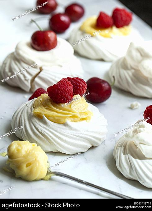 Individual meringues topped with lemon curd, raspberries, whipped cream and cherries