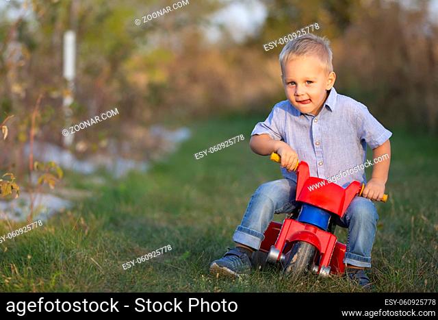 A little boy on a red motorcycle rides on the green grass