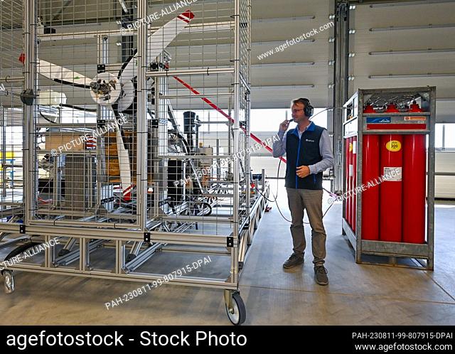 11 August 2023, Brandenburg, Strausberg: Alexander Behrens, development engineer at APUS GmbH, stands next to a hydrogen aircraft engine he developed