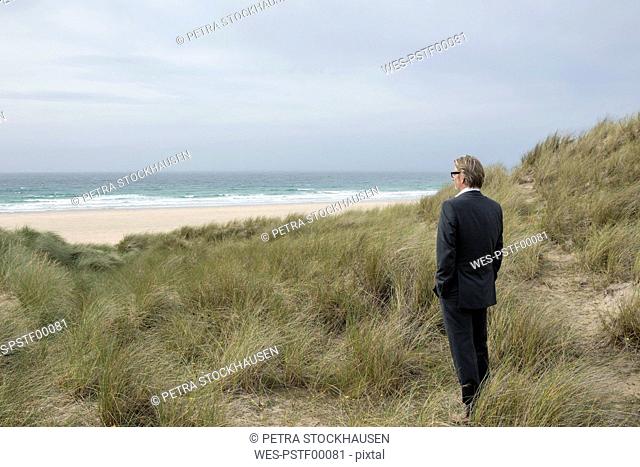 UK, Cornwall, Hayle, businessman standing in beach dunes looking at view