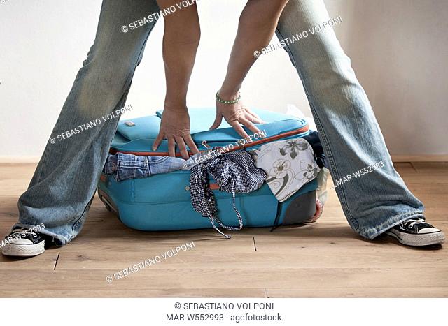 woman trying to close her suitcase