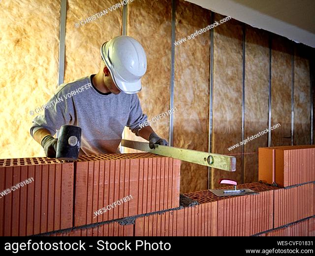 Bricklayer with hammer using spirit level on bricks at construction site