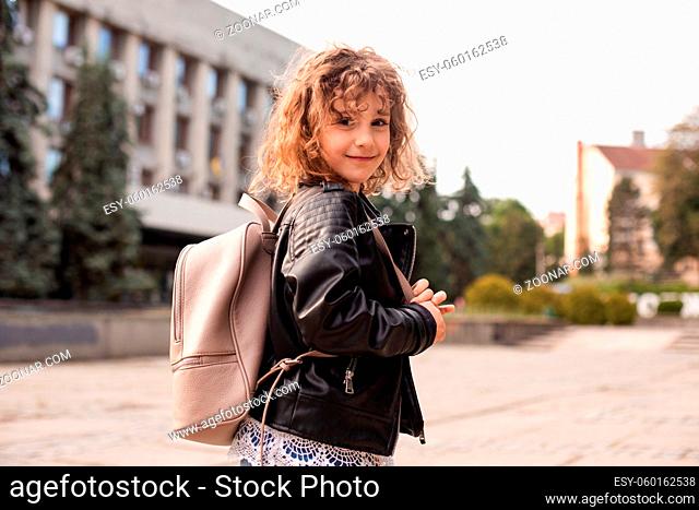Portrait of the happy girl with curly hair and stylish clothes. She walks around the city with a bag and looks at the camera