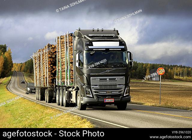 Black customised Volvo FH16 750 truck pulls full timber trailer along Highway 52 under dramatic autumnal sky. Salo, Finland. October 11, 2019