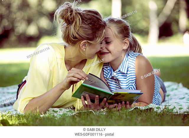 Happy girl and young woman with book lying on blanket in a park