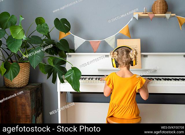 Girl listening music on headphones and playing piano at home