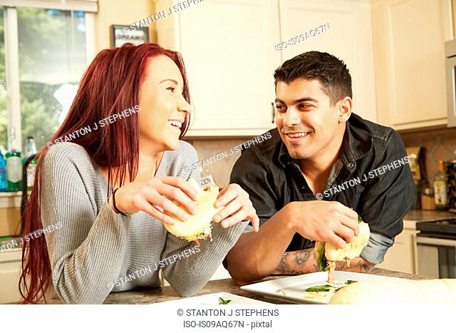 Young couple eating sandwiches at kitchen counter