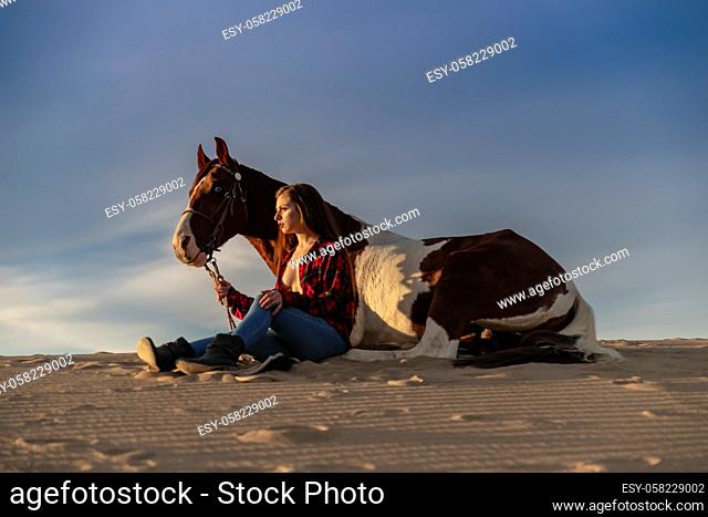 A young brunette female spends time with her horse in a desert environment