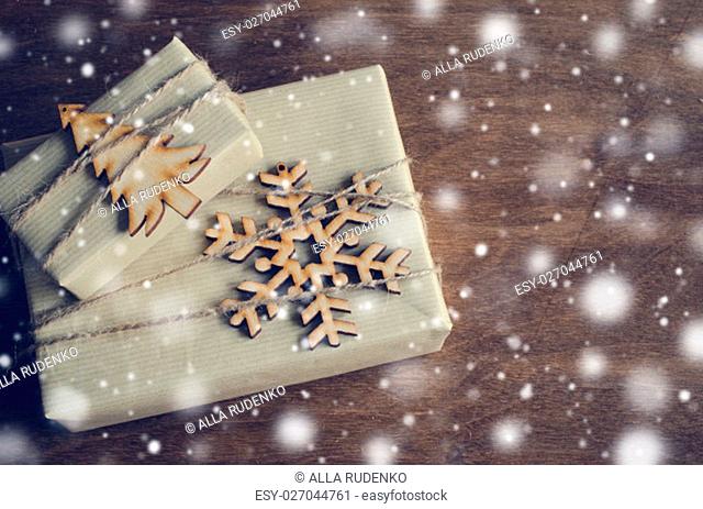 Kraft Boxes with Gifts Decorated with Wooden Snowflake, Christmas Tree and Jute on Wooden Background. Vintage Image with Drawn Snowfall