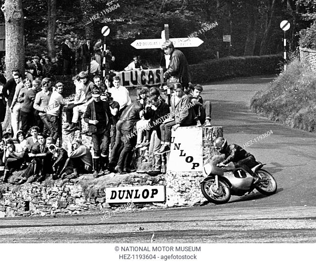 Ultra-Lightweight TT race, Isle of Man, 1966. Spectators occupy whatever vantage point they can find as Hugh Anderson crosses Governors Bridge on his Suzuki 125...