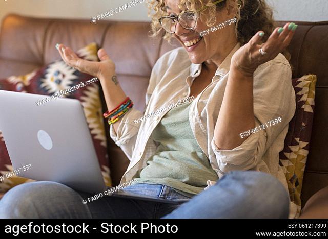 Surprised and overjoyed happy young woman with laptop computer sitting on the sofa- video call with friends online - cheerful people using internet technology...