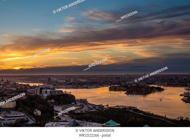 Scenic view of lake and residential district against cloudy sky during sunset