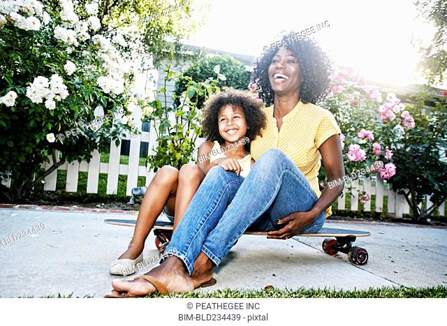 Smiling mother and daughter sitting on skateboard