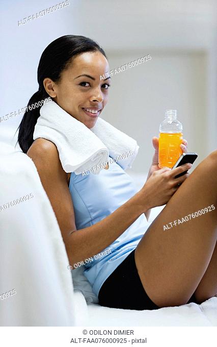 Young woman holding sports drink and cell phone