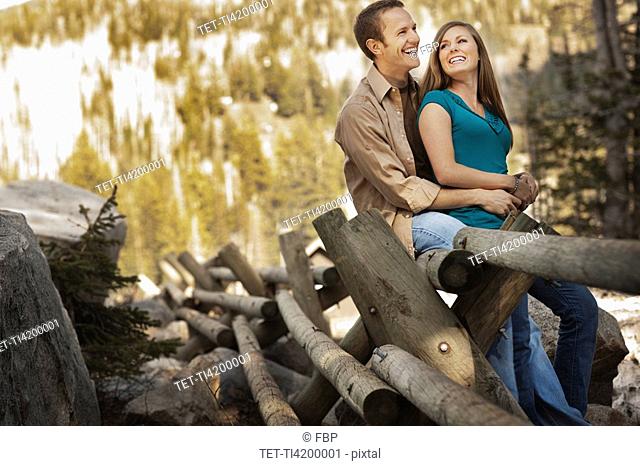 Laughing couple sitting on log fence