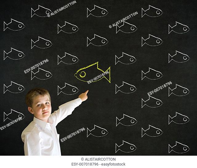 Pointing boy dressed up as business man with independent thinking chalk fish swimming against the flow on blackboard background