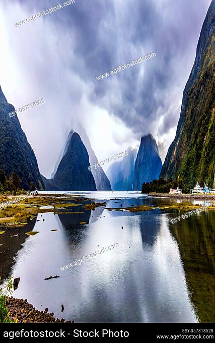Storm clouds cover the sky. Mirror-smooth water of the Milford Sound fjord reflects mountains. Magic country of fantastic heroes. New Zealand