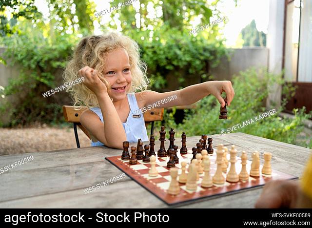 Smiling girl playing chess in garden