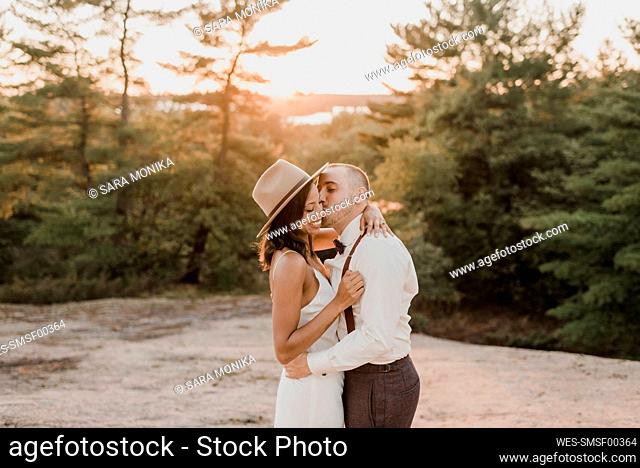 Couple kissing while standing on walkway in forest during sunset