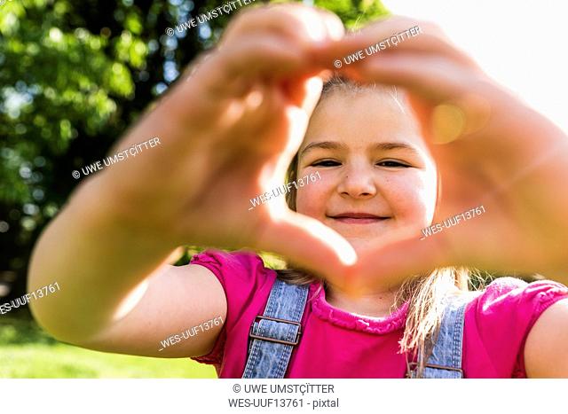 Portrait of smiling girl shaping a heart with her hands in park